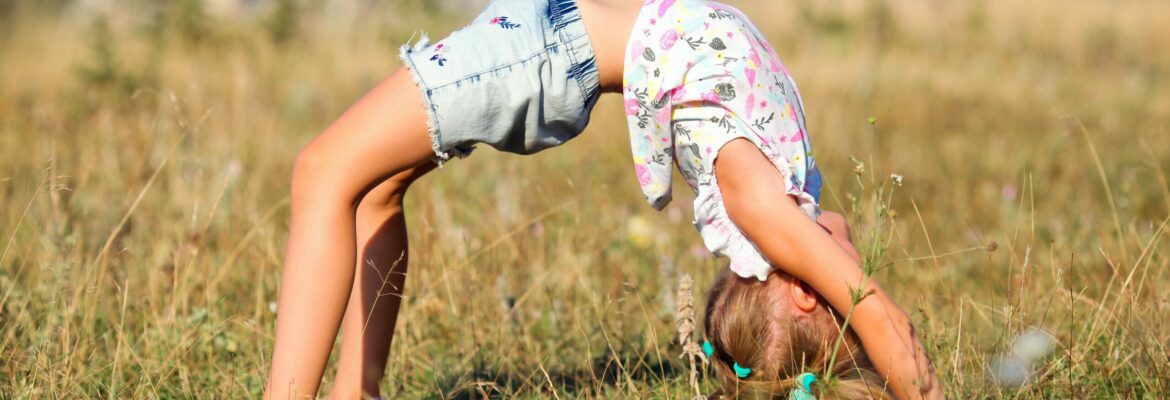 Bewegungsspiele im Kindergarten, Bewegen in der Kita, Kind macht Brücke auf dem Rasen