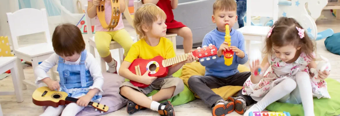 Eine Gruppe von Kindern sitzt in einer Kita auf dem Boden. Sie halten verschiedene Instrumente in den Händen und üben das Musizieren.