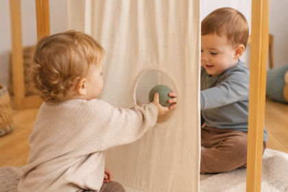 Zwei Kleinkinder reichen sich einen Ball durch eine runde Öffnung in einem Stofftuch.