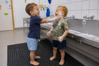 Zwei Kleinkinder stehen am Waschbecken und spielen mit Seife.