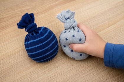 Kinderhand drückt einen kleinen, mit Stoff gefüllten Sockenbeutel auf einem Holztisch.