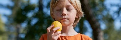 Kind hält mit geschlossenen Augen eine gelbe Frucht in der Hand.
