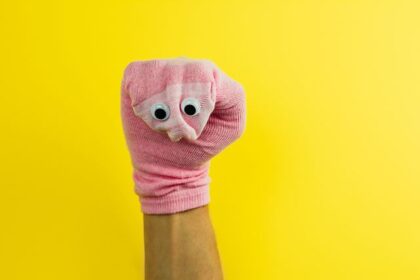 Rosa Sockenpuppe mit Wackelaugen vor gelbem Hintergrund.