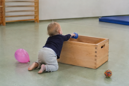 Kleinkind schiebt einen blauen Ball in eine Holzkiste.
